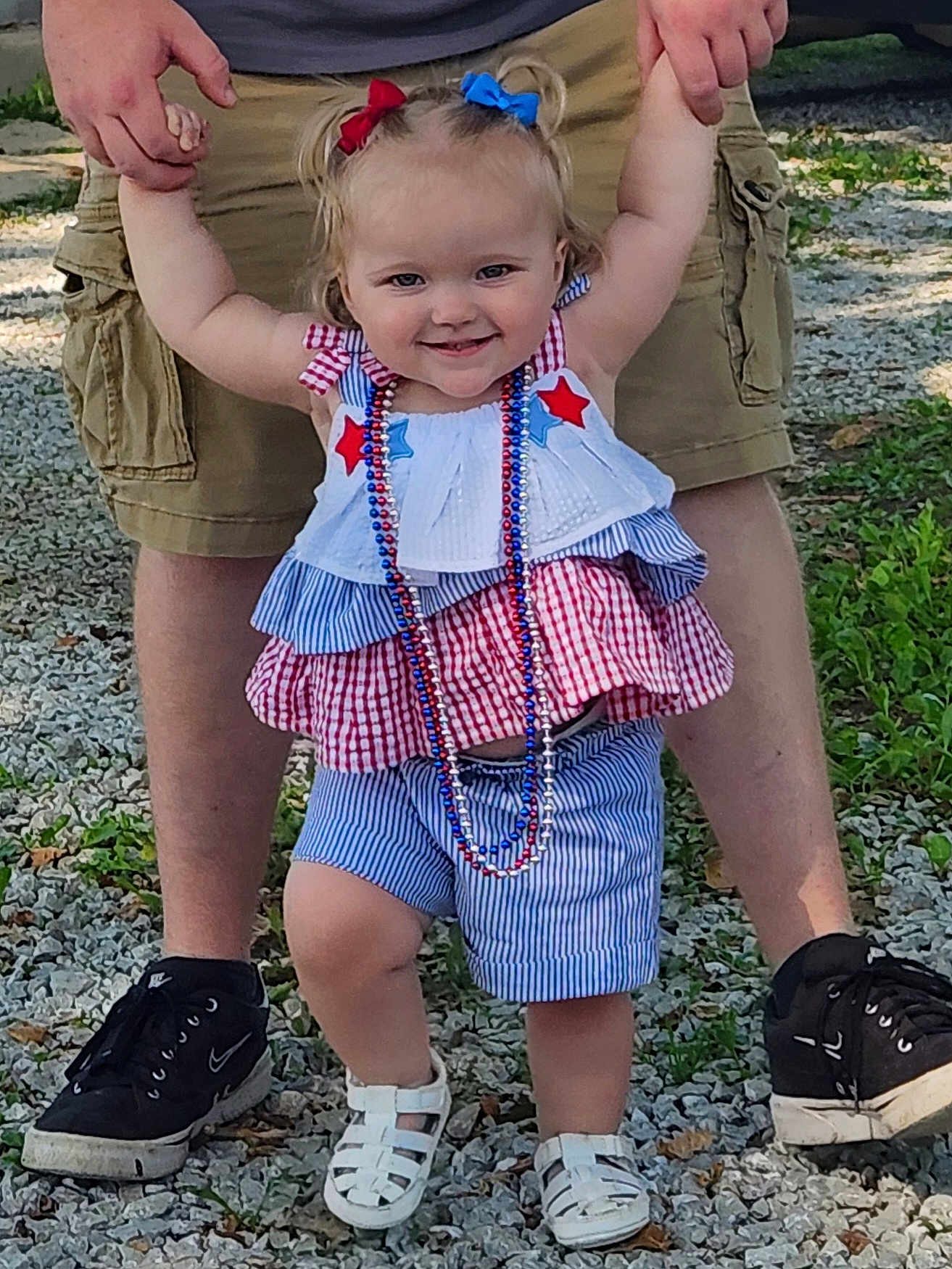 Olivianah is registered to the contest to win money with this photo: toddler, child, person, smiling, outdoor, gravel, shorts, sneakers, holding_hands, hair_bows, necklace, summer_clothing, happy, walking, legs, adult, blue, red, white, beads