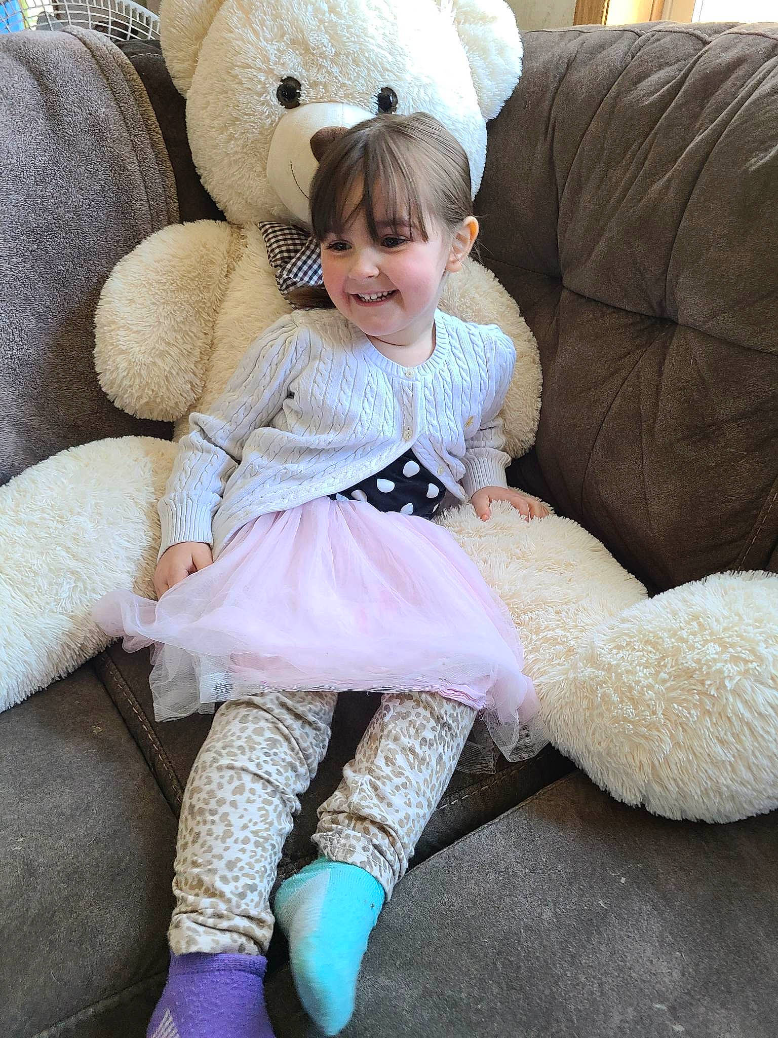 Sophia is registered to the contest to win money with this photo: baby_toddler_clothing, child, comfort, couch, face, foot, fur, happy, hat, human_leg, joy, knee, lap, person, sitting, smile, sock, sun_hat, teddy_bear, textile