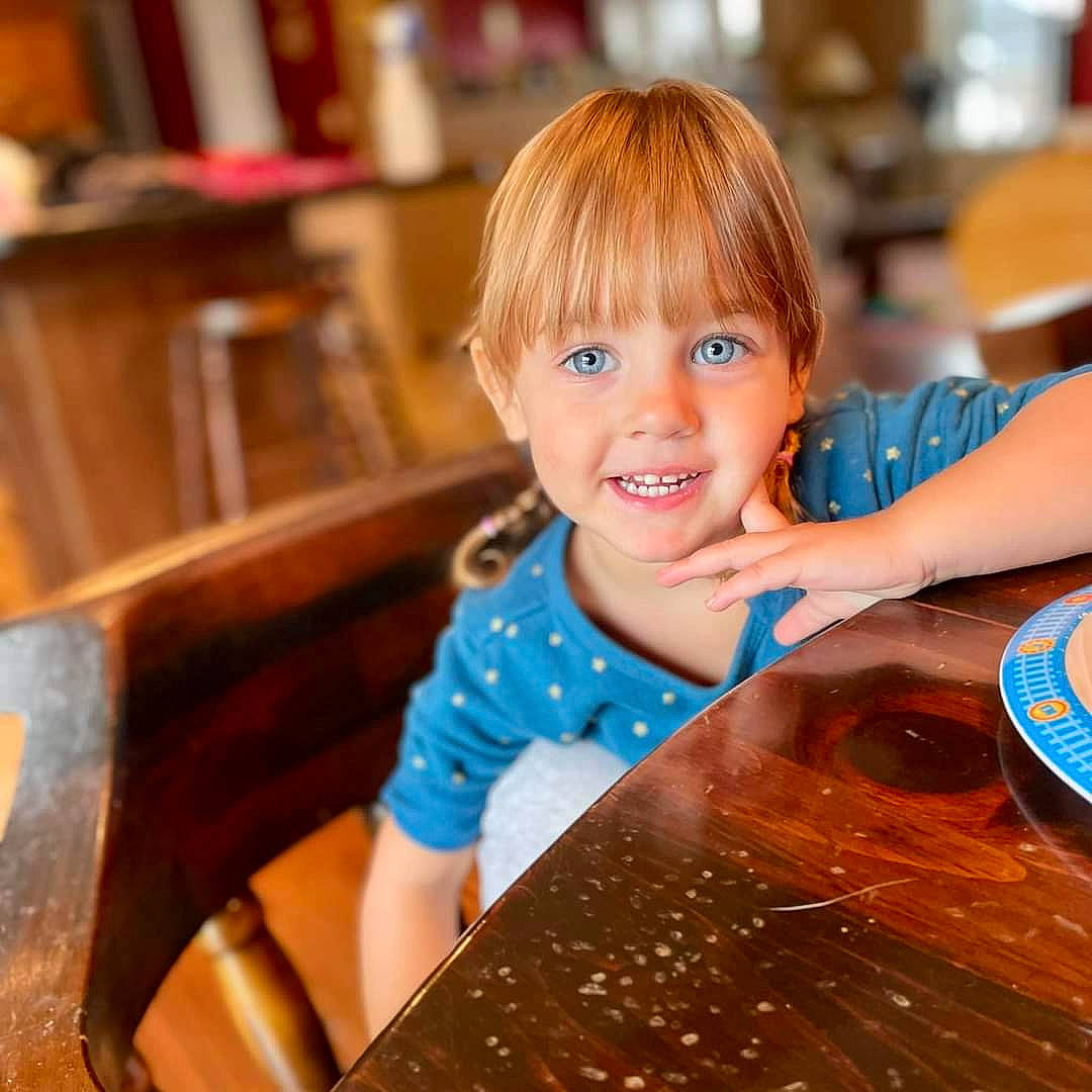 Cora is registered to the contest to win money with this photo: brown_hair, chair, child, flooring, fun, furniture, happy, hardwood, joy, leisure, person, recreation, room, shelf, sitting, smile, table, tableware, toddler, varnish