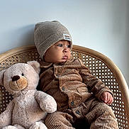 Djibril participe au concours pour gagner de l'argent avec cette photo : baby, child, teddy_bear, beanie, corduroy, pajamas, wicker_chair, plush_toy, carpet, indoor, cozy, cute, portrait, sitting, soft_toy, warm_clothing, infant, floor, neutral_background, expression