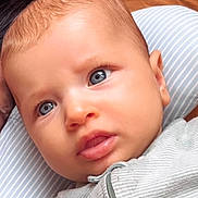 Hannah a rejoint le concours — aidez-le/la à gagner de superbes lots ! baby, blue_eyes, close_up, curious_expression, face, infant, laying_down, striped_outfit, striped_pillow, soft_texture, young_child, portrait, skin, head, person, child, indoor, cute, expression, human