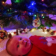 Auguste a rejoint le concours — aidez-le/la à gagner de superbes lots ! baby, infant, child, smiling, christmas_tree, christmas_lights, ornament, bokeh, festive, red_pajamas, lying_down, cozy, holiday, decoration, closeup, face, ear, blanket, home_interior, soft_lighting