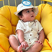 Mahir joined the competition — help win amazing prizes! baby, infant, child, yellow_chair, cushion, hat, romper, fruit_print, sitting, cute, indoor, portrait, skin, face, hand, foot, clothing, curious, young, comfortable