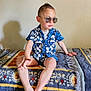 Kilian participe au concours pour gagner de l'argent avec cette photo : barefoot, blue_shirt, boy, casual, child, confident, cool, fashion, home, indoor, mohawk, patterned_blanket, portrait, relaxed, short_hair, shorts, sitting, sunglasses, wall, young