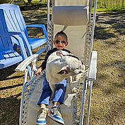 Kilian participe au concours pour gagner de l'argent avec cette photo : blue_pants, bulldog, casual, chair, child, dog, fence, grass, outdoor, pet, playful, recliner, relaxing, shadow, shoes, smile, sunglasses, sunny, tree, white_dog