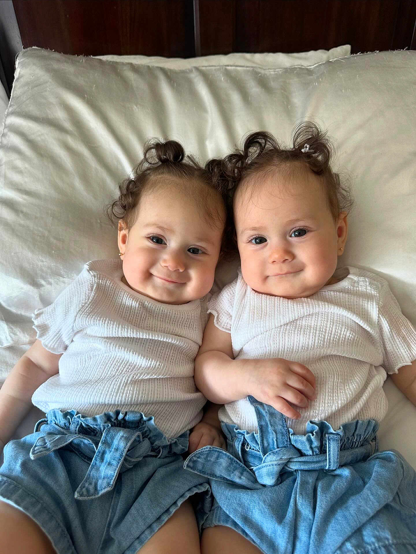 Anahi And Areli joined the competition — help win amazing prizes! baby, twins, curly_hair, white_shirt, denim_shorts, pillow, smile, cute, infant, child, toddler, adorable, lying_down, matching_outfits, happy, portrait, indoor, soft_lighting, closeup, face