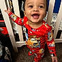 toddler, child, pajamas, red_clothing, smiling, baby, crib, nursery, carpet, bed, furniture, indoor, person, happy, standing, hand, face, cute, cartoon_print, closeup