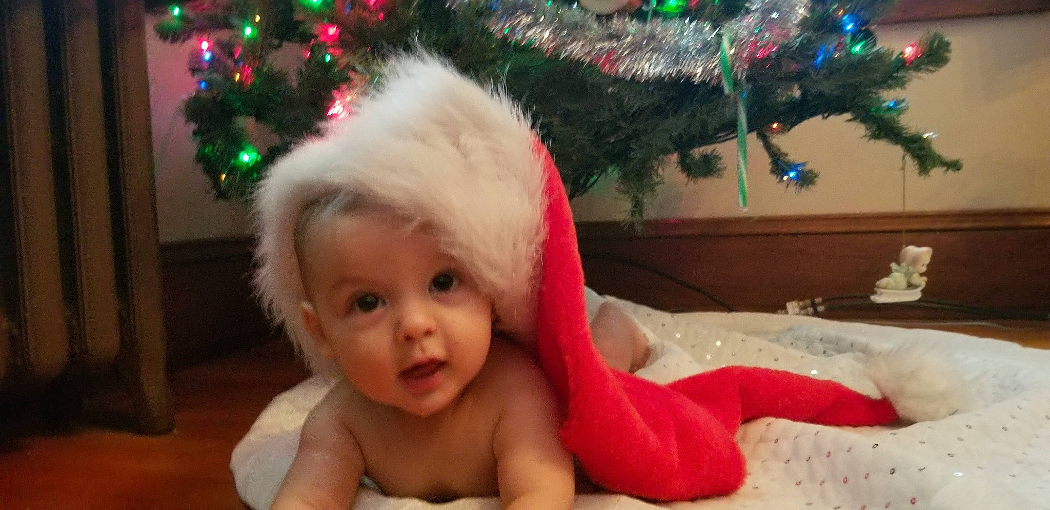 Dennis is registered to the contest to win money with this photo: baby, cheek, child, christmas, christmas_decoration, christmas_eve, christmas_ornament, christmas_tree, event, fun, head, holiday, mouth, person, play, sitting, smile, toddler