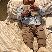 Amir joined the competition — help win amazing prizes! baby, infant, child, beanie, bib, blanket, brown_pants, clothing, cute, face, hand, indoors, laying_down, person, plush, relaxing, shoes, socks, wood_floor, warm_colors