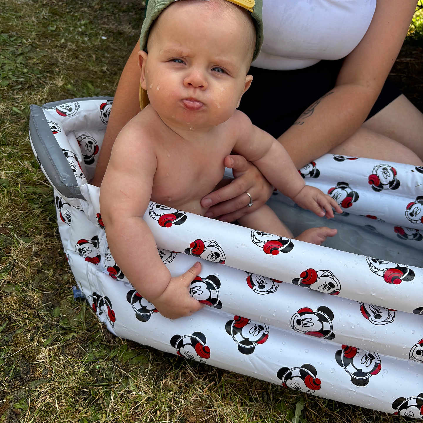 Isaïah a rejoint le concours — aidez-le/la à gagner de superbes lots ! arm, baby, cap, child, clothing, cute, expression, funny_face, grass, hand, inflatable_pool, mickey_mouse, outdoor, person, skin, summer, sunlight, support, tattoo, water