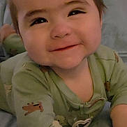 Mateo is registered to the contest to win money with this photo: baby, infant, child, portrait, smiling, face, eyes, brown_hair, pajamas, green_clothing, animal_print, sitting, bed, bedding, indoors, home, close_up, happy, adorable, pacifier