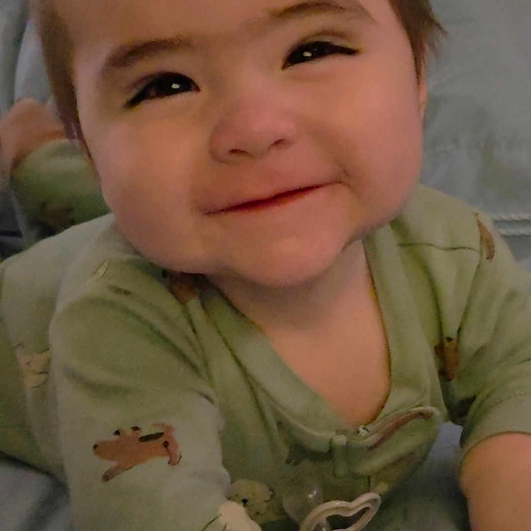 Mateo is registered to the contest to win money with this photo: baby, infant, child, portrait, smiling, face, eyes, brown_hair, pajamas, green_clothing, animal_print, sitting, bed, bedding, indoors, home, close_up, happy, adorable, pacifier