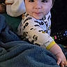 Mateo is registered to the contest to win money with this photo: baby, child, infant, smiling, portrait, indoor, blanket, blue_blanket, onesie, clothing, remote_control, plush_toy, adult, face, eyes, hair, sitting, cozy, home, photography