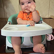 Mateo joined the competition — help win amazing prizes! baby, infant, highchair, orange_shirt, waving, cute, smiling, indoor, feeding, child, person, seat, plastic_tray, sippy_cup, floor, tile_wall, hand, foot, expression, home