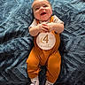 baby, infant, smiling, clapping, romper, mustard, blue_blanket, lying_down, cute, happy, child, face, hands, feet, socks, indoors, portrait, closeup, expression, young