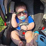 Mateo is registered to the contest to win money with this photo: baby, baby_toy, blue_shirt, casual, child, cloth, cute, foot, grip, hand, infant, outdoor, pacifier, relaxed, seatbelt, shade, stroller, sunglasses, sunlight, toy