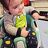 Mateo is registered to the contest to win money with this photo: toddler, child, baby, smiling, sitting, high_chair, indoor, portrait, face, brown_hair, clothing, shirt, pajamas, cartoon, monster, letters, living_room, television, furniture, happy