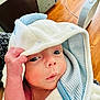 baby, infant, hooded_towel, hand, face, eyes, skin, indoor, wooden_floor, furniture, curious, child, person, cute, newborn, wrapped, soft_texture, striped_towel, closeup, portrait