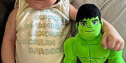 Kase joined the competition — help win amazing prizes! baby, child, plush_toy, hulk, green, onesie, clothing, couch, pillow, infant, cute, smiling, face, person, indoor, soft_toy, relaxing, lying_down, expression, furniture