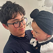 Israa participe au concours pour gagner de l'argent avec cette photo : child, baby, glasses, black_headwrap, white_shirt, black_clothing, balloons, celebration, party, holding, indoor, face, person, portrait, happy, curly_hair, young, interaction, smiling, toddler