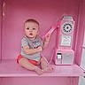 baby, child, phone_booth, pink, rotary_phone, vintage_phone, sitting, curious, toy, indoor, person, telephone, communication, retro, cute, infant, holding, expression, casual_clothing, background