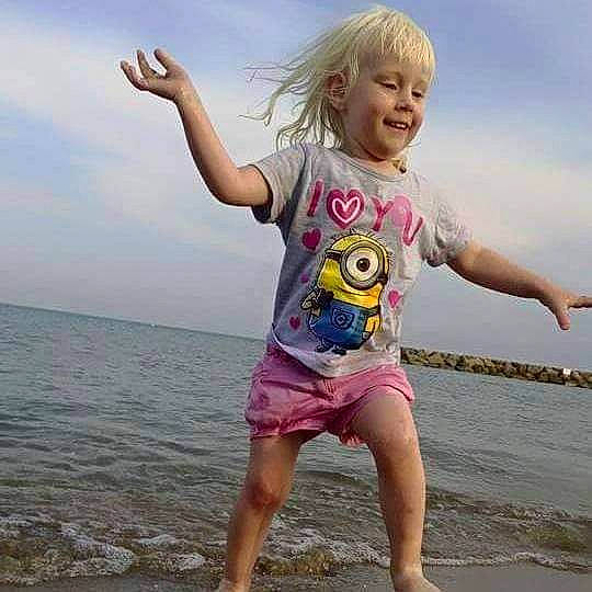 Loréline participe au concours pour gagner de l'argent avec cette photo : barefoot, beach, body_of_water, cloud, cool, fun, gesture, happy, joy, leisure, people_in_nature, people_on_beach, person, shoulder, sky, sleeve, smile, t_shirt, thigh, toddler