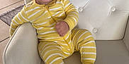 Jordan is registered to the contest to win money with this photo: baby, child, smiling, yellow_onesie, striped_clothing, chair, cushion, blue_blanket, indoor, tile_floor, happy, person, face, seated, cute, infant, home, cozy, comfort, portrait