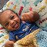 Elijah is registered to the contest to win money with this photo: baby, smiling, blue_shirt, knitted_blanket, colorful_blanket, indoor, happy, infant, person, cute, child, face, hand, furniture, couch, cozy, portrait, playful, expression, young