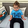 toddler, child, boy, blue_shirt, black_pants, sitting, outdoor_furniture, cushion, pillow, happy_fall, pumpkin, fall_decor, funny_face, hair_tuft, portrait, cute, smirk, casual_clothing, bench, daylight