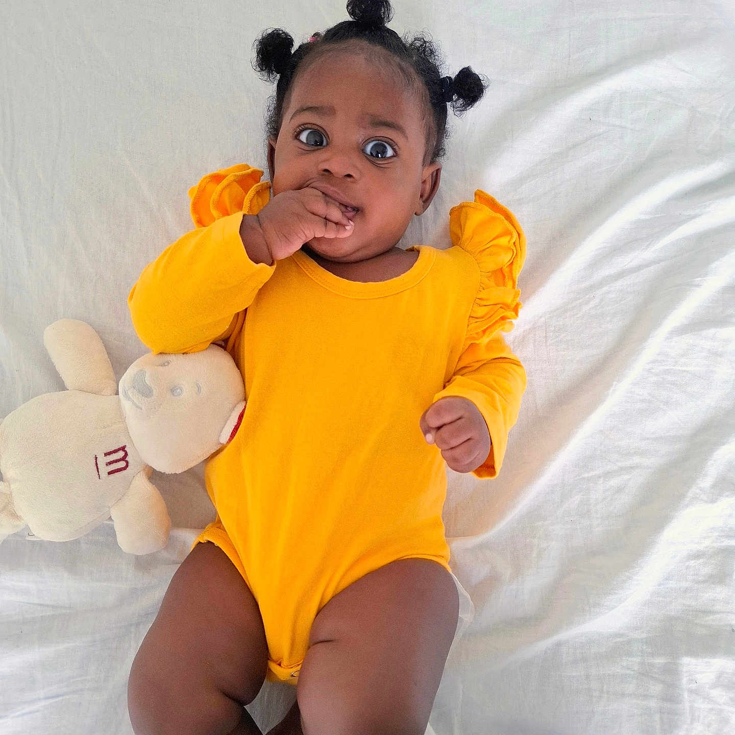 Hernelle participe au concours pour gagner de l'argent avec cette photo : baby, baby_girl, bed, casual, child, curious_expression, cute, dark_skin, hair_buns, hand_in_mouth, indoors, infant, lying_down, one_person, portrait, relaxed, soft_toy, stuffed_animal, white_bedspread, yellow_clothing