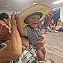 Kayden is registered to the contest to win money with this photo: toddler, child, hat, smile, happy, indoor, people, adult, group, floor, wooden_floor, shirt, holding, sitting, casual, room, light, furniture, joy, fun