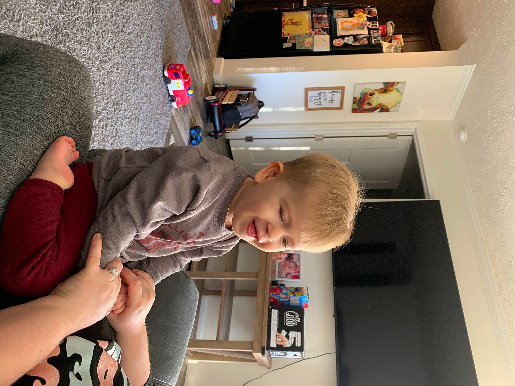 Wyatt is registered to the contest to win money with this photo: arm, baby, child, comfort, elbow, flooring, foot, fun, human_leg, knee, person, play, room, sandal, shelf, shelving, t_shirt, thigh, toddler
