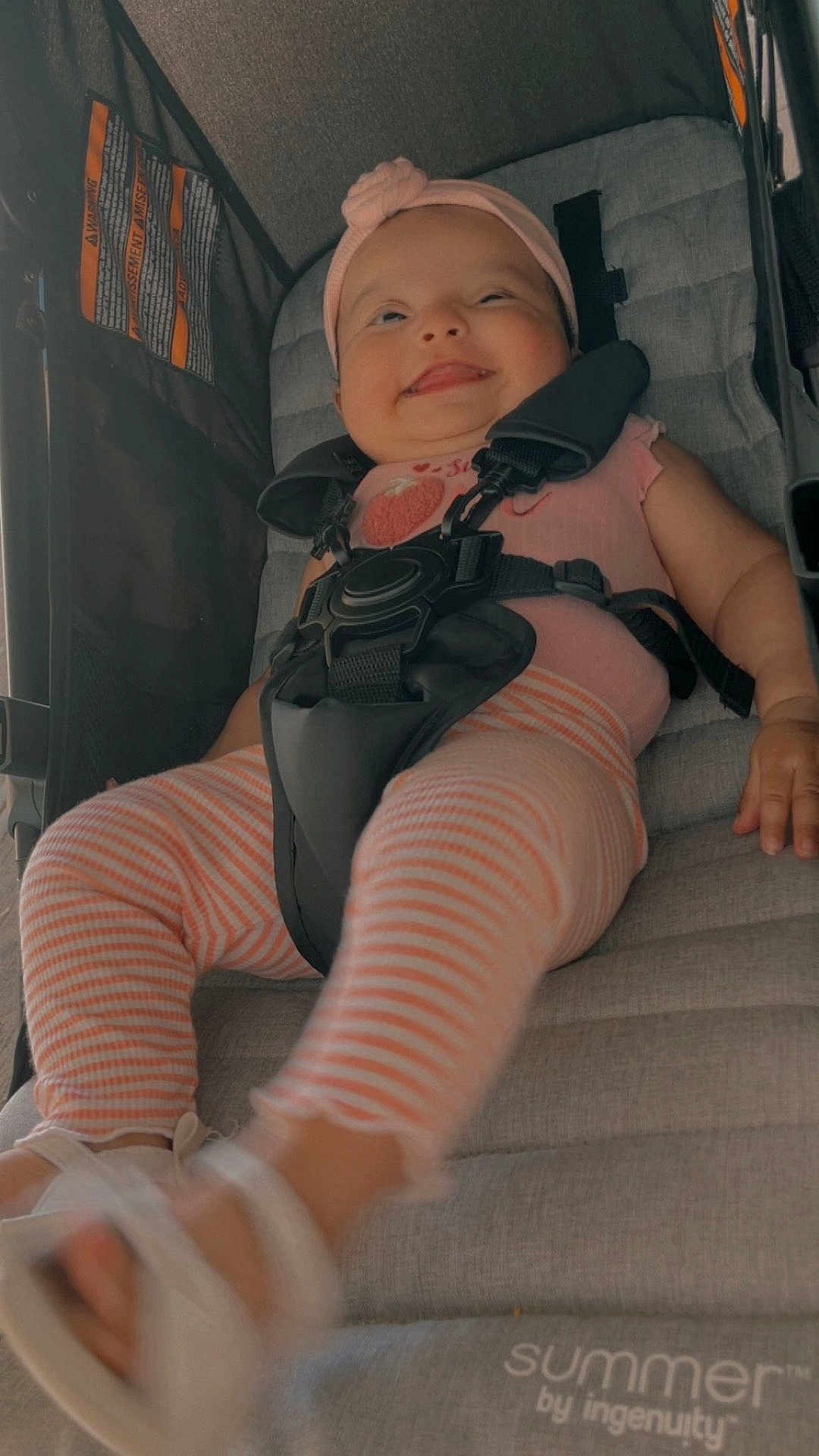 Brenda is registered to the contest to win money with this photo: baby, baby_clothes, child, comfort, cute, footwear, happy, headwear, infant, outdoor_gear, person, pink_headband, playful, safety_harness, sandal, seat, seatbelt, smiling, striped_leggings, stroller