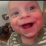 Ian is registered to the contest to win money with this photo: baby, close_up, smiling, indoor, child, face, joyful, striped_clothing, furniture, wall_decoration, head, person, portrait, happy, infant, young_child, room, blurred_background, cheerful, expression