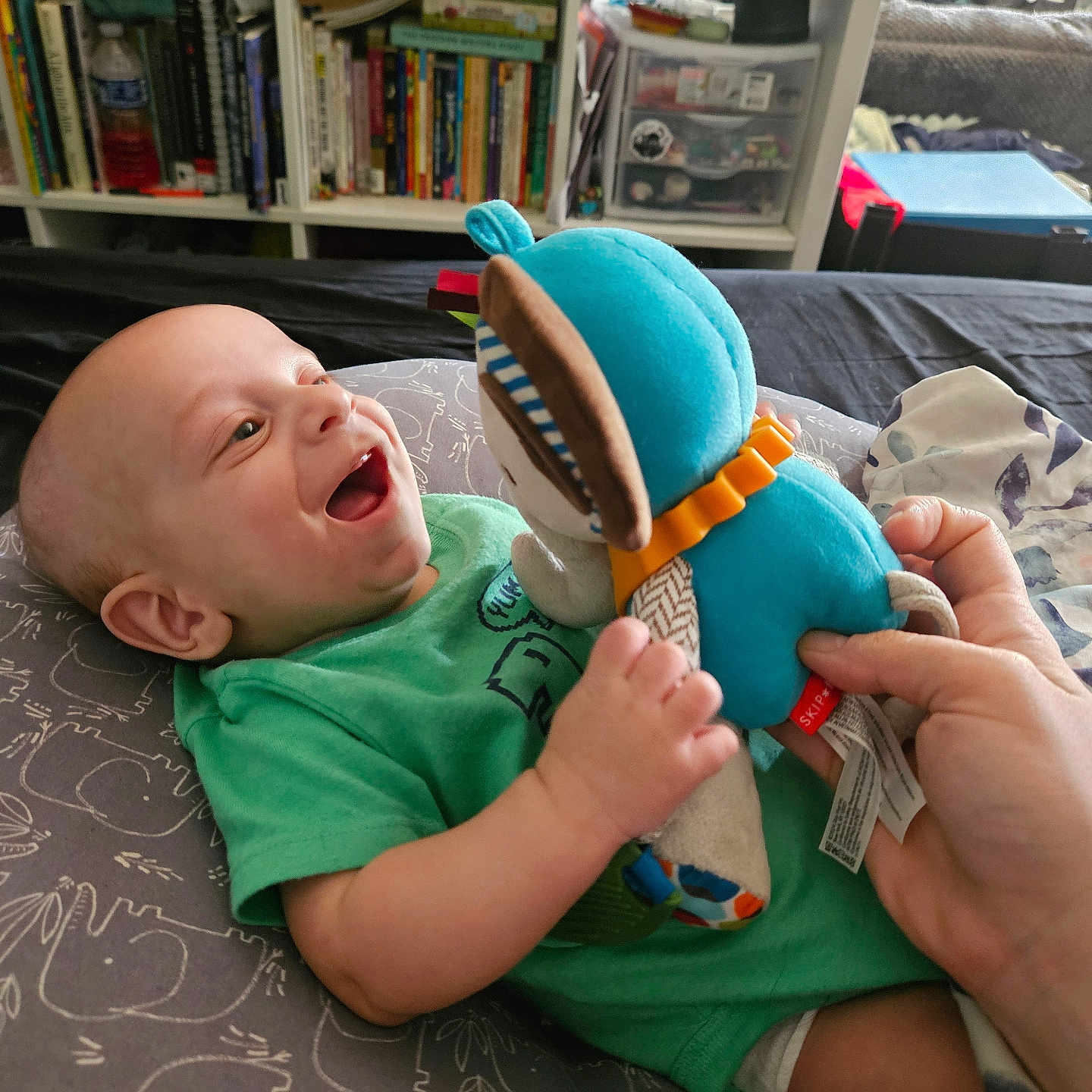 Ian joined the competition — help win amazing prizes! baby, bedroom, books, bookshelf, child, cuddly, furniture, green_shirt, hand, happy, home, indoor, infant, person, pillow, playful, plush_toy, relaxing, smiling, toy