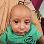 Ian is registered to the contest to win money with this photo: baby, child, face, eyes, green_shirt, speech_bubble, text_graphic, person, adult_arm, holding, close_up, indoor, skin, expression, cute, infant, head, clothing, seated, background_blur