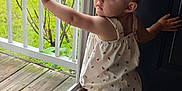 Scarlett is registered to the contest to win money with this photo: baby, toddler, child, standing, barefoot, hair_bow, sundress, window, glass, porch, railing, lawn, wooden_floor, door, looking_back, curious, portrait, hand, face, balcony
