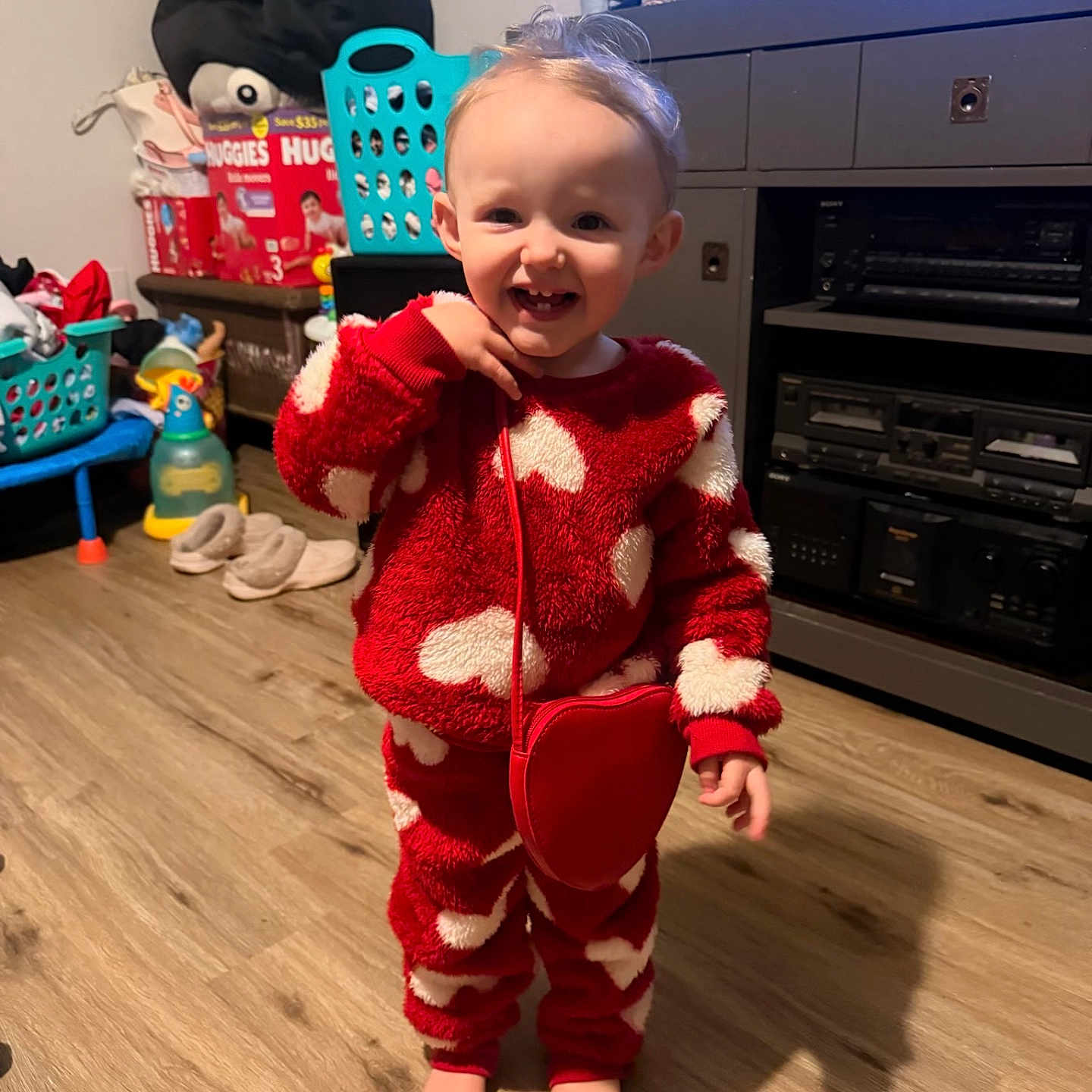 Scarlett is registered to the contest to win money with this photo: barefoot, child, cute, diapers_box, dresser, furniture, heart_pattern, indoors, laundry_basket, living_room, pajamas, person, portrait, red_purse, slippers, smile, television, toddler, toys, wood_floor