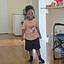 child, indoor, smiling, tshirt, shorts, toy, floor, wooden_floor, living_room, kitchen, furniture, person, happy, playtime, socks, home, young_child, standing, casual_clothing, afro_hair