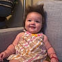 baby, smiling, plaid_dress, couch, indoor, happy, child, bracelet, hair_spike, infant, person, seated, cute, chubby, skin, furniture, portrait, button, fabric, colorful