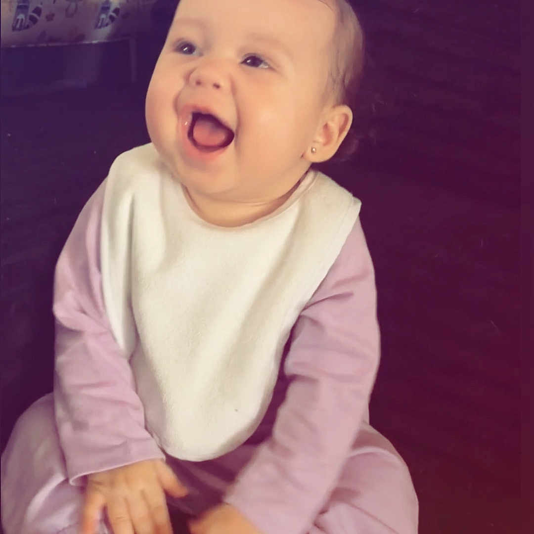 Khalani joined the competition — help win amazing prizes! baby, child, infant, smiling, laughing, portrait, sitting, pink_outfit, bib, bow, indoor, cozy, happy, face, hands, shoes, white_shoes, long_sleeves, baby_clothing, candid_photo