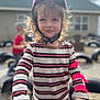Piper is registered to the contest to win money with this photo: child, helmet, striped_shirt, outdoor, playground, scooter, bike, person, young_child, smile, curly_hair, play, daylight, hand, toy, protective_gear, blurred_background, casual_clothing, fun, active