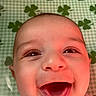 baby, smiling, happy, face, infant, child, green_background, shamrocks, closeup, portrait, red_light, white_clothing, skin, mouth_open, eyes, lying_down, indoors, cute, cheerful, banner_ad