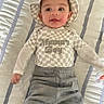 baby, child, smiling, hat, checkered_pattern, shirt, mamas_boy_text, pants, lying_down, bedspread, striped, cute, tongue_out, happy, infant, person, clothing, indoor, portrait, headwear