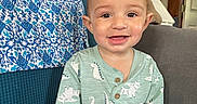 Tymeir joined the competition — help win amazing prizes! toddler, child, smile, remote_control, curly_hair, dinosaur_print, green_clothing, sitting, couch, blue_couch, indoor, happy, cute, person, home, furniture, lamp, fabric, pattern, room