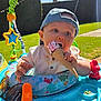 baby, ice_cream, cap, outdoor, sunlight, baby_walker, toy, grass, hedge, summer, blue_sky, child, cute, eating, cone, playtime, sunshine, smiling, colorful, fun