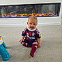 Matteo joined the competition — help win amazing prizes! baby, child, soccer_uniform, carpet, fireplace, indoor, floor, person, maroon, navy, socks, toy, modern, living_room, reflection, cute, tongue_out, shirt, shorts, warm_lighting