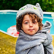 Louie joined the competition — help win amazing prizes! child, towel, curly_hair, pool, outdoor, blanket, hooded_towel, greenery, portrait, cute, face, young_child, wrapped, summer, water, soft_texture, expression, person, nature, daytime