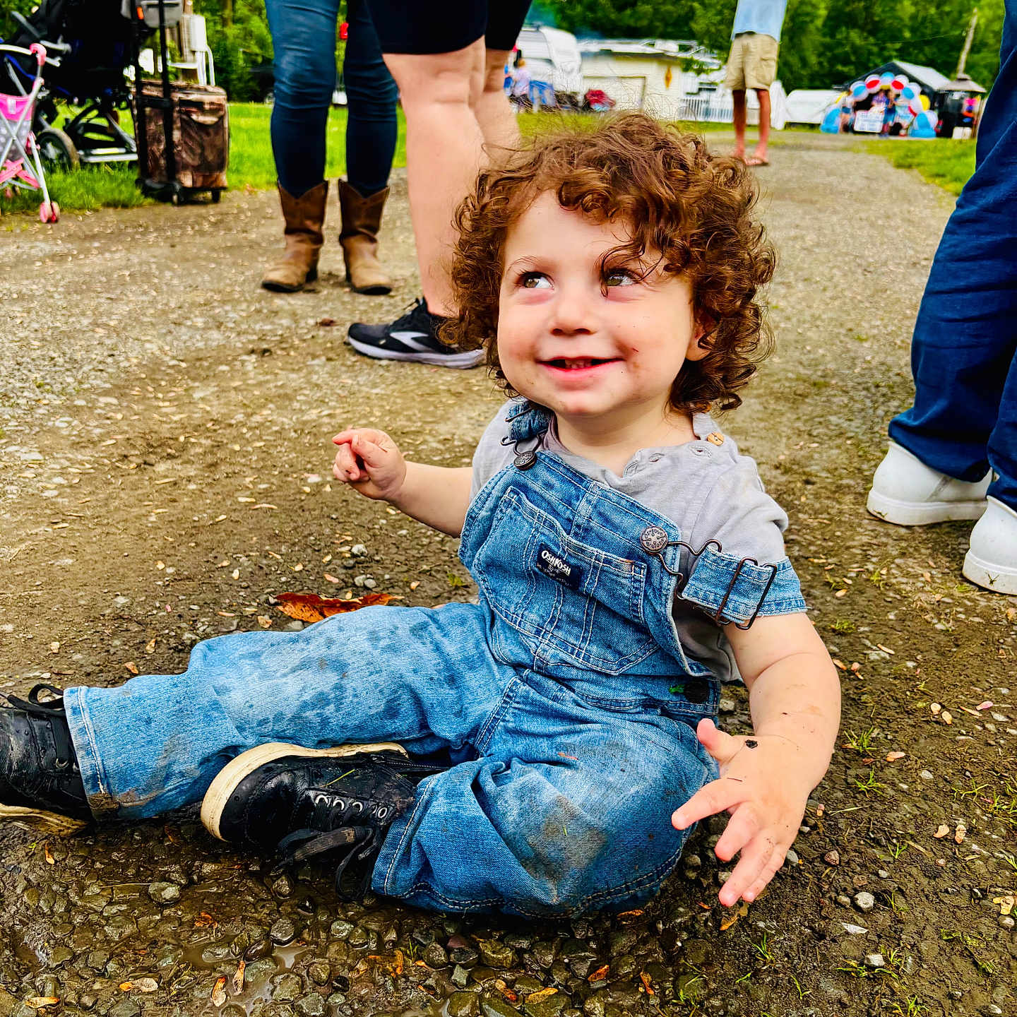 Louie joined the competition — help win amazing prizes! boots, casual_clothing, child, curly_hair, daylight, denim_overalls, grass, gravel_path, happy, legs, muddy_clothes, nature, outdoor, people, playful, puddle, shoes, smiling, toddler, trees