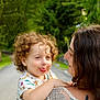 child, toddler, curly_hair, woman, adult, outdoor, nature, trees, greenery, road, holding, playful, tongue_out, white_clothing, lace, tattoo, smile, portrait, family, affection